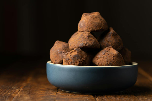 Dark chocolate truffles in a bowl on a wooden surface — rich, moody food photography