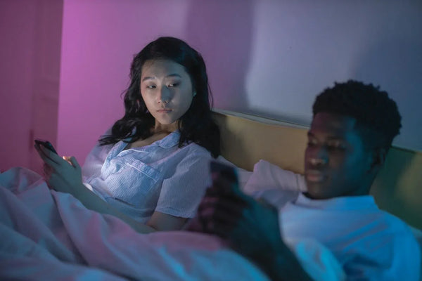 Couple in bed using smartphones together โ digital intimacy and connection for modern couples