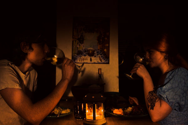 A couple share a glass of wine by lamplight at a small table