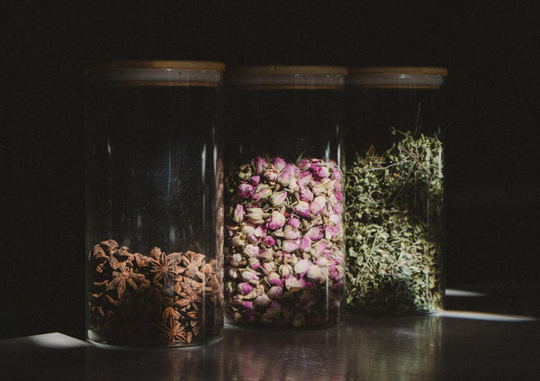 Glass jars containing star anise, dried rosebuds, and botanical herbs — natural aphrodisiac ingredients