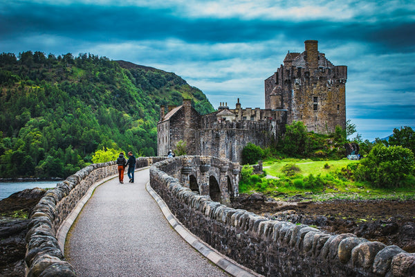 A couple walk across the stone bridge to Eilean Donan Castle in the Scottish Highlands