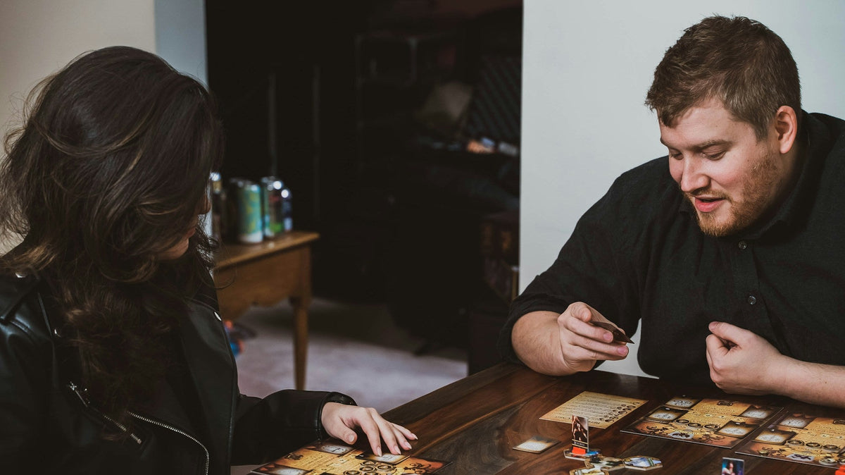 A couple sit at a wooden table playing a board game together at home