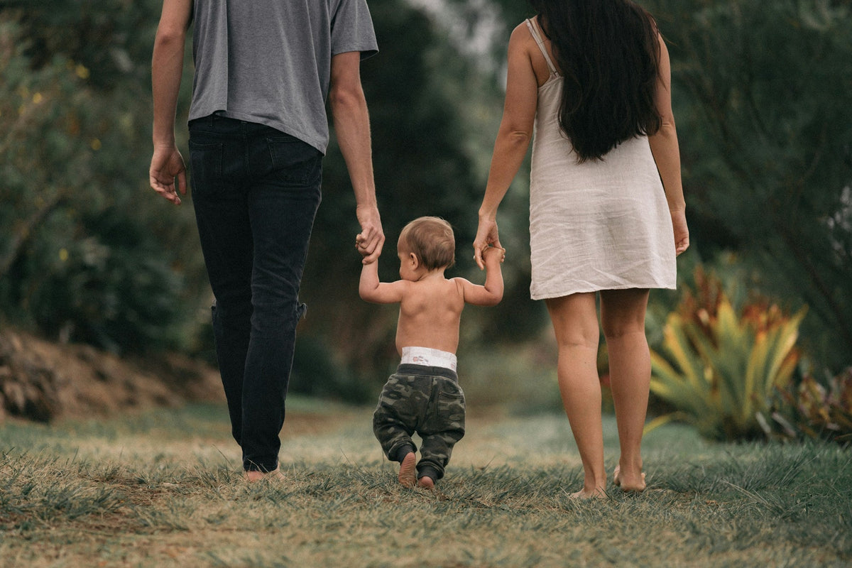 Parents walking barefoot across a garden, holding hands with their toddler between them