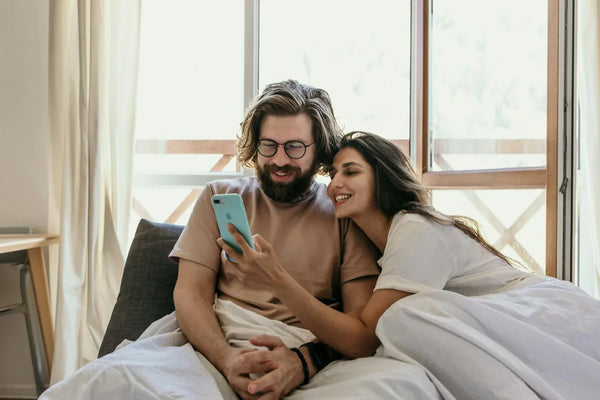 Content couple sharing a relaxed morning in bed while looking at a smartphone together