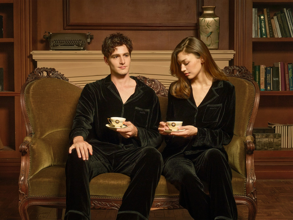 A couple in matching dark pyjamas share tea on a vintage sofa