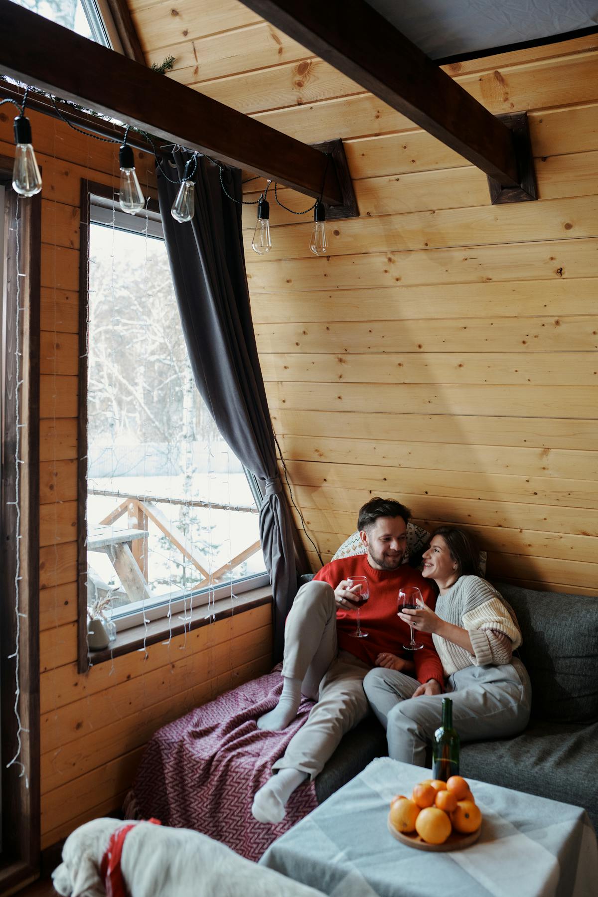 Couple cuddled up on a couch in a winter cabin with red wine
