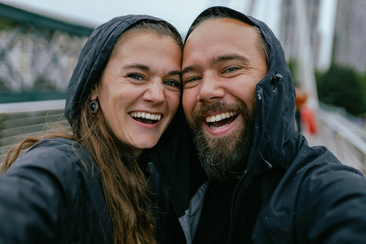 A couple in rain jackets press their faces together and grin at the camera